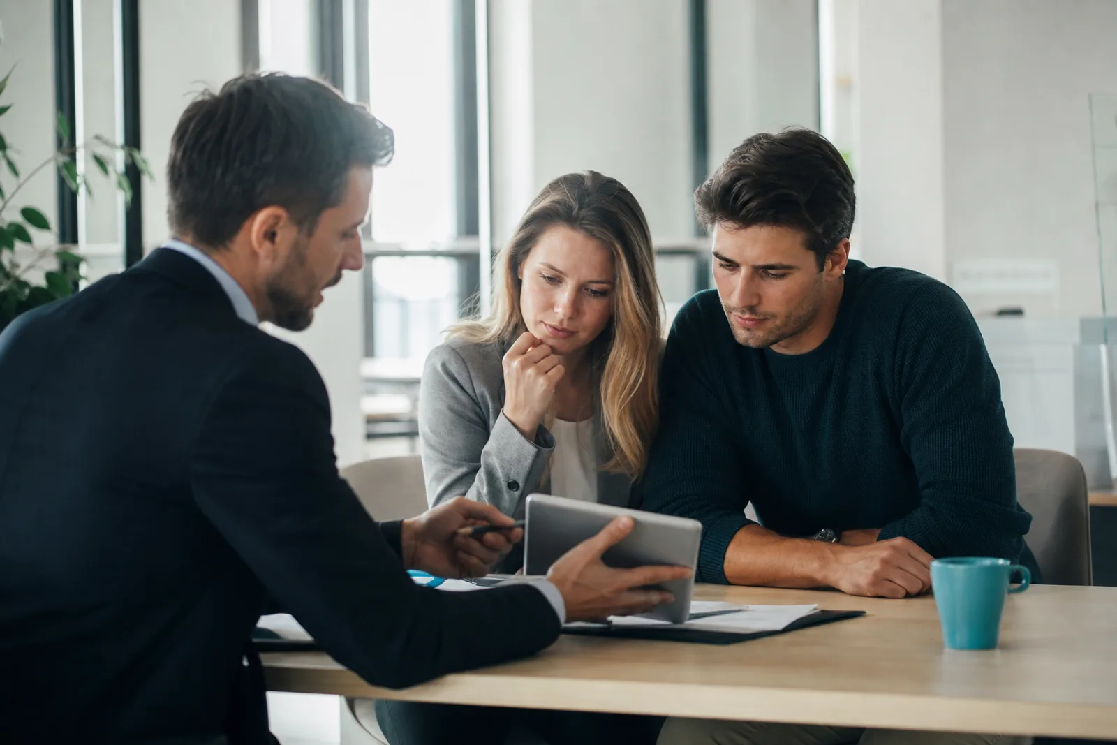Jeune couple consultant des documents de prêt immobilier avec un conseiller bancaire dans une agence lumineuse.