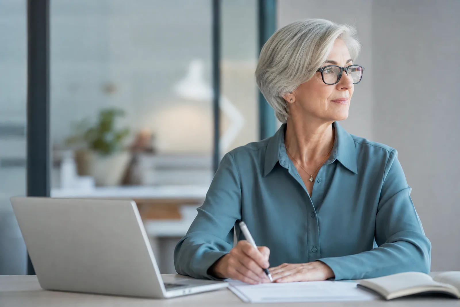 Personne retraitée travaillant sereinement sur un ordinateur portable dans un bureau lumineux, entre vie active et retraite.
