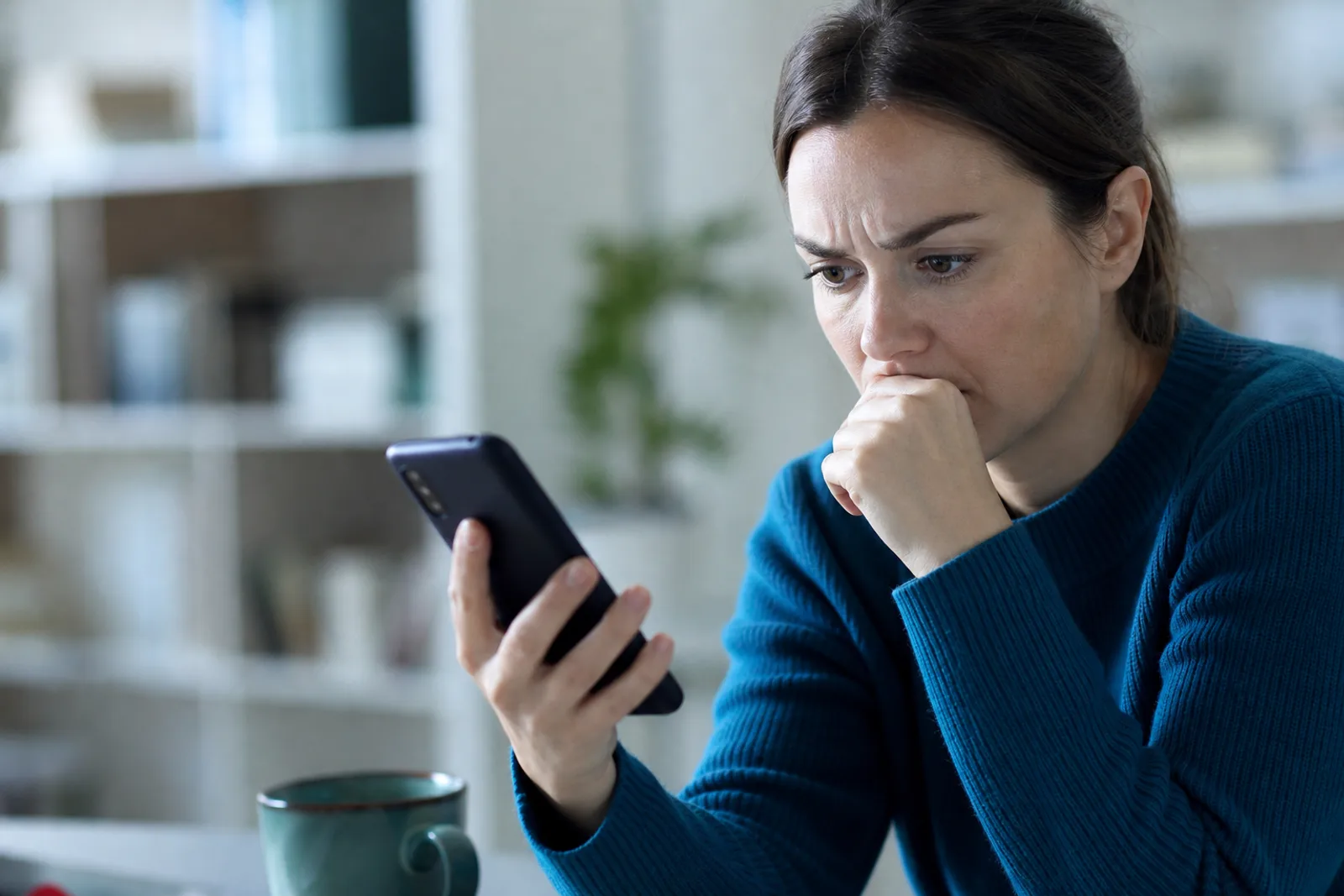Personne inquiète regardant son smartphone affichant une perte de réseau, dans un intérieur lumineux.