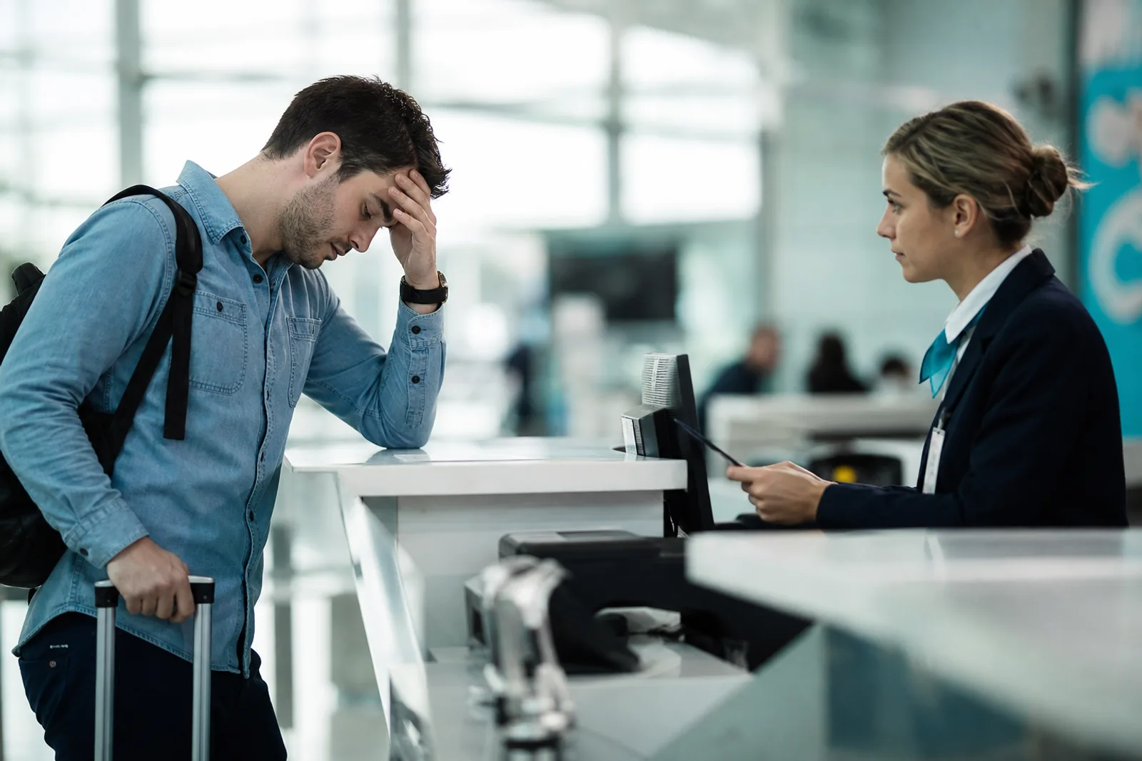 Passager dépité, valise à la main, face à une agente au comptoir d'enregistrement d'un aéroport.