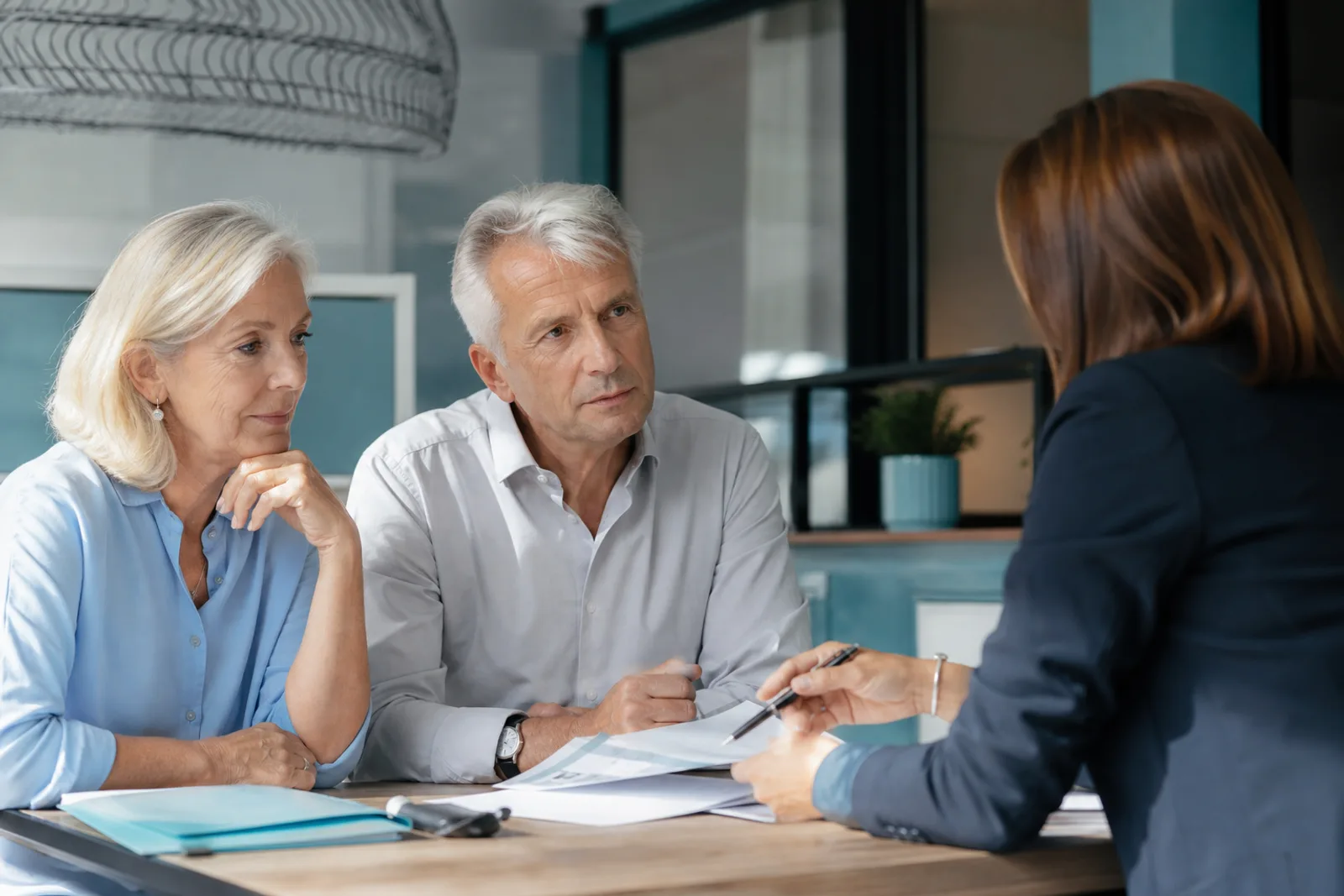 Couple senior en rendez-vous avec une conseillère, documents contractuels sur la table.