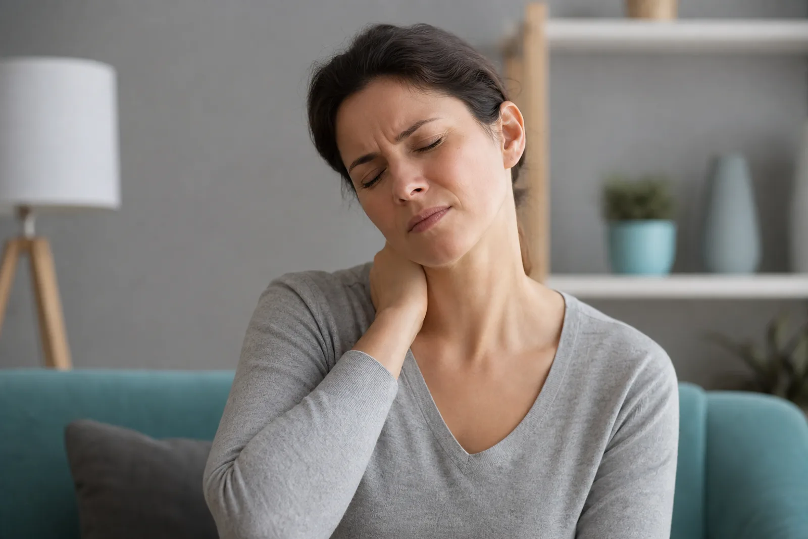 Femme se tenant la nuque avec une expression de douleur, assise sur son canapé.